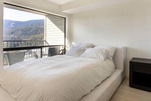 Cama blanca en habitación con ventana grande en Amazing Views 2 BR/2 BA Ski In Ski Out Condo en Whistler