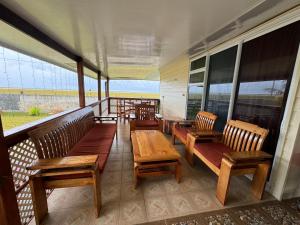 eine Veranda mit Holzbänken, Tischen und Fenstern in der Unterkunft Toamanahere Guesthouse in Tubuai