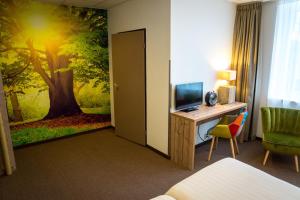 Habitación de hotel con escritorio, TV y un mural de árboles. en Forest Hotel en Den Helder