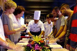 een groep mensen die rond een chef staan om eten te bereiden bij Mila Cruises in Ha Long
