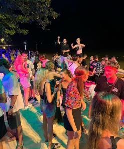 um grupo de pessoas de pé na areia em uma festa em Blanco Beach Bar Hostel em Phi Phi Don