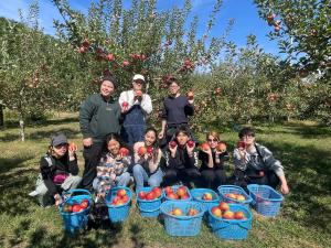 um grupo de pessoas num pomar de maçãs com cestos de maçãs em みんなでつくるふるさとウエダイラハウス 