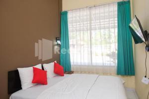 um quarto com uma cama com almofadas vermelhas e uma janela em Travelista Homestay near GOR Candradimuka Semarang Mitra RedDoorz em Srondolwetan
