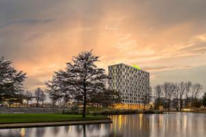 a tall building next to a lake with a tree at ibis Styles Rotterdam Ahoy in Rotterdam