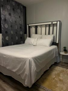 uma cama com lençóis brancos e almofadas num quarto em Windhoek City Center self catering appartment em Windhoek