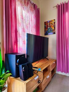 a flat screen tv on a wooden stand with pink curtains at Serene 2BR Escape: Poolside Bliss in Iloilo City in Iloilo City