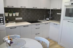 une cuisine avec des armoires blanches, une table et un évier dans l'établissement Двухкомнатная квартира на самом берегу реки, à Pavlodar