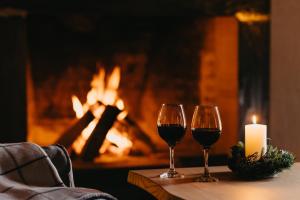 two glasses of wine and a candle on a table with a fireplace at Alpina Hotel in Gudauri