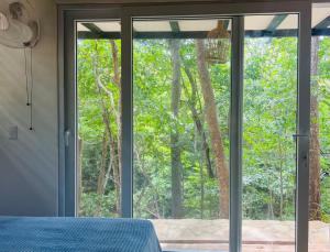 a bedroom with sliding glass doors looking out at the forest at Agora at Playa Maderas - Surf House, Cabanas and Casitas in Playa Maderas