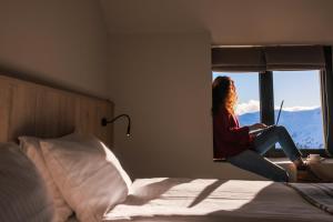 una mujer sentada en una cama mirando por la ventana en Alpina Hotel, en Gudauri