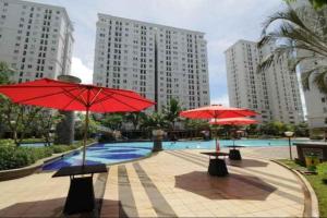 two tables with red umbrellas in a pool with buildings at Apartemen kalibata city by Rama Property in Jakarta