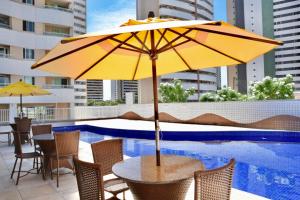 einen Tisch mit einem Sonnenschirm neben einem Pool in der Unterkunft Condomínio Zaragoza no Parque Del Sol in Fortaleza
