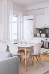 a white kitchen with a wooden table and white chairs at Nordic Design Apartment City Center in Rovaniemi