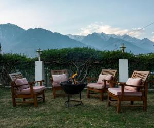 vier Stühle und eine Feuerstelle mit Bergen im Hintergrund in der Unterkunft The Wooden Chalet, Manali by DBP in Manali