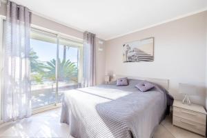 a white bedroom with a bed and a large window at LE MIDI 8 by ESTATES CANNES in Cannes