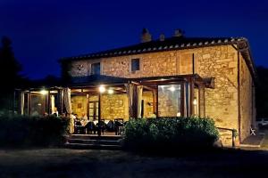 a stone house with tables and chairs outside at night at Antico Casale Pozzuolo in Seggiano