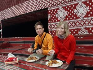 a man and woman sitting on a bench with plates of food at Calm Camp in Wadi Rum