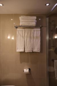 La salle de bains est pourvue d'une douche et de serviettes blanches sur un portant. dans l'établissement Dreamtel London Kensington, à Londres