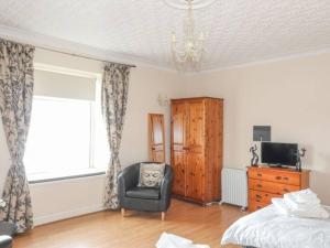 a bedroom with a bed and a chair and a window at Sea Front Spacious Apartment on Anglesey in Brynsiencyn