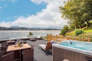 a hot tub on a patio next to a body of water at Sea Front Spacious Apartment on Anglesey in Brynsiencyn