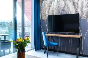 - un salon avec une télévision et une chaise bleue dans l'établissement Aparts4U - Kras Resort Apartament A302 z prywatnym jacuzzi, sauną i widokiem na góry, à Szklarska Poręba