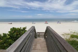 a wooden boardwalk leading to a beach with people at Ground floor beachfront with steps to the beach and pool & beach access in New Smyrna Beach