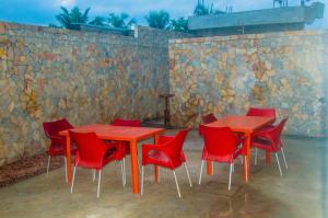 um grupo de mesas e cadeiras vermelhas em frente a uma parede de pedra em Résidence Roma em Cotonou