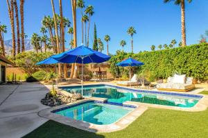 ein Pool mit blauen Sonnenschirmen im Hof in der Unterkunft Palm Oasis #2993 in Palm Springs