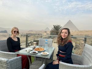 two women sitting at a table in front of the pyramids at Blue Scarab Pyramids View in Cairo