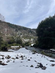 a river with snow on the ground and trees at Cabañas Los Huemules in Malalcahuello