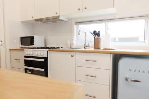 cocina con armarios blancos, fregadero y microondas en Sweet beautiful TINY HOME with pool and 2 minute drive to the beach, en Wollongong