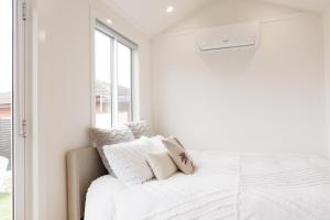 a white bedroom with a bed and a window at Sweet beautiful TINY HOME with pool and 2 minute drive to the beach in Wollongong
