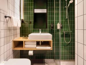 baño de azulejos verdes con lavabo y ducha en ibis Styles Copenhagen Orestad, en Copenhague