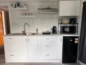 a kitchen with white cabinets and a sink and a microwave at Hill View Abode Tawa in Wellington