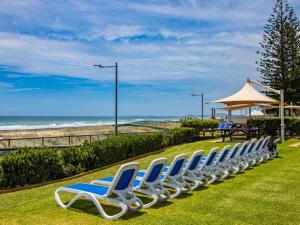 una fila di sedie blu e bianche sedute sull'erba vicino alla spiaggia di Breakers North Absolute Beachfront Apartments a Gold Coast