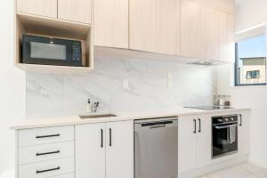 a white kitchen with white cabinets and a microwave at Cozy Brand New Townhouse 20 in Auckland