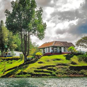 a house on top of a hill next to the water at El Trebol in Guatapé