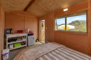 Habitación pequeña con cama y ventana en Karo Hut A - Ninety Mile Beachfront Cabin en Awanui