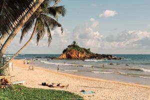 a beach with palm trees and people on the beach at Bisandu guesthouse in Mirissa