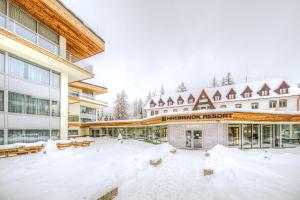 a building covered in snow with benches in front of it at Grand Apartments Hrebienok in Starý Smokovec