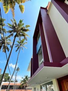 a purple building with palm trees in the background at BAVA Lalitha Retreat Center Varkala in Varkala