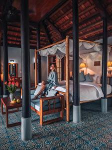 une femme assise sur un lit dans une chambre dans l'établissement Pilgrimage Village Boutique Resort & Spa, à Hue