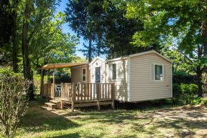 a white cabin with a porch in the woods at Camping les Avignon - la Laune in Villeneuve-lès-Avignon