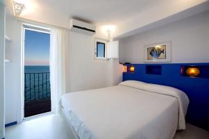 una camera con un letto bianco e una grande finestra di Hotel Saraceno a Giglio Porto