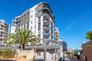 a tall white building with palm trees in front of it at Apartamento Melior 2C - PlusHolidays in Calpe