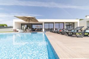 a swimming pool with chairs and an umbrella at Villa Bahia in Aldeia do Meco