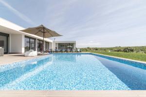 a swimming pool with an umbrella next to a house at Villa Bahia in Aldeia do Meco