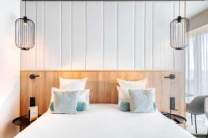 a bedroom with a bed with white sheets and blue pillows at GOLDEN TULIP LYON OUEST TECHLID Hotel & Spa in Limonest