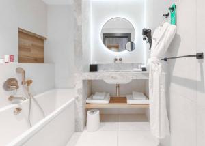 een badkamer met een wastafel, een bad en een spiegel bij GOLDEN TULIP LYON OUEST TECHLID Hotel & Spa in Limonest
