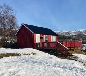 a red house with a deck in the snow at Aurora House Dåfjord/Tromsø in Karlsøy